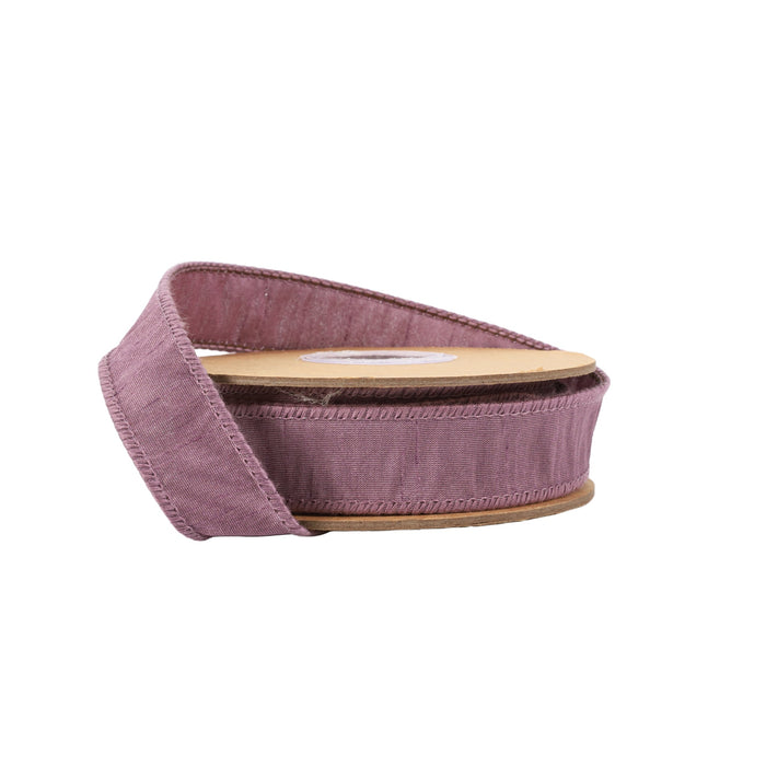 The 1" Amethyst Dupioni Ribbon 9100W-473-25E features stitched edges, a subtle sheen, and comes partially unrolled on a round cardboard core.