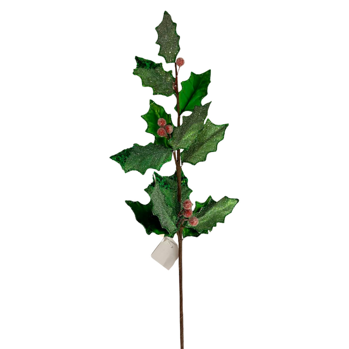 The 27" Green and Red Metallic and Sugared Holly Leaves and Berries Spray 32231 showcases emerald green leaves with a glossy, glittery finish and small red berries, all attached to a brown stem adorned with a white tag at the base.