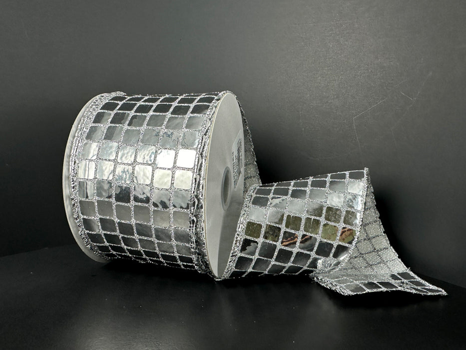 A roll of 2.5X10Y Silver Discoball Sequins Ribbon (41533-40-16) sits against a dark background, partially unrolled to reveal its shiny, mirror-like surface with a grid of silver squares, reminiscent of a disco ball.