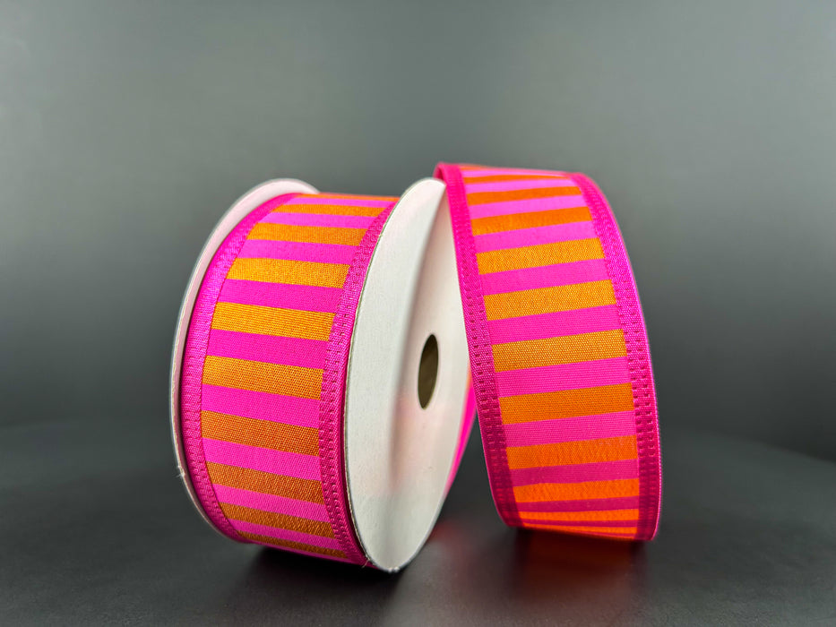 Two spools of the 1.5X10Y Fuchsia Satin-Orange Stripes/Orange Edge Ribbon are displayed upright, elegantly wrapped around white cylindrical cardboard holders against a dark backdrop.