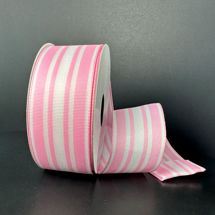 Partially unrolled, the 1.5X10Y White Pink Modern Ticking Ribbon (47507-09-03), featuring alternating pink and white vertical stripes, rests against a dark background. The ribbon is wide and has a smooth texture.