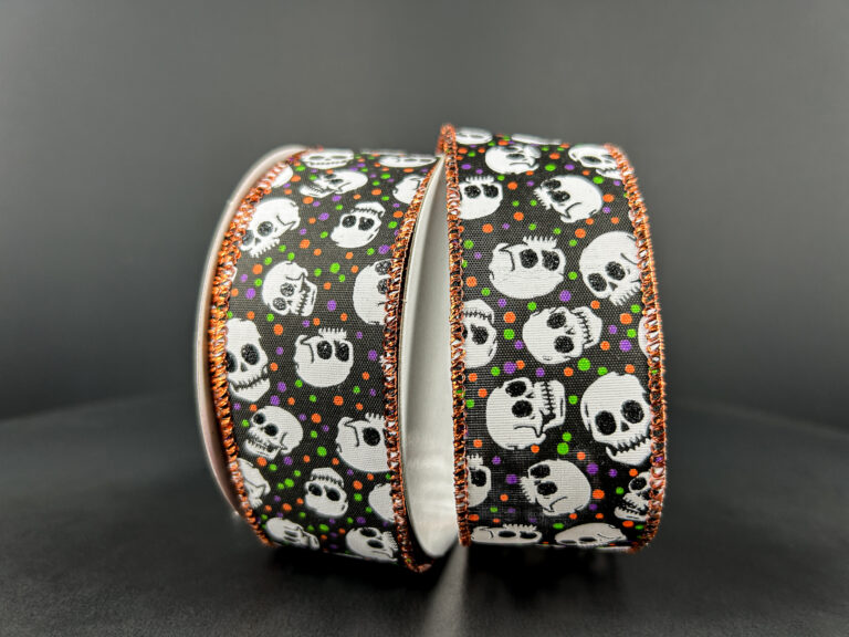 Two 1.5X10Y black satin ribbons, each adorned with white skulls, colorful dots, and edge-accented in orange stitching, are arranged against a dark background.