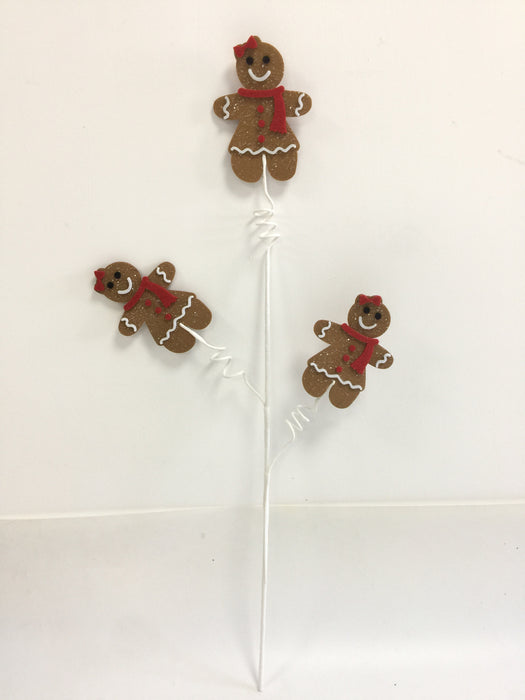 The 29 Long Brown Gingerbread Lady Spray 65252 features three festive gingerbread ladies with red bows and scarves on white wire stems, arranged bouquet-style against a white background—ideal for holiday displays.