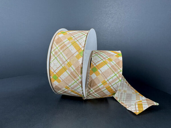 A 1.5X10Y Ivory Moss Mustard Brown Argyle Plaid Ribbon (65525-09-35), featuring a tan, yellow, green, and white plaid pattern, sits on a dark surface with the ribbon partially unrolled and extending outward.