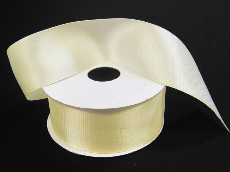 A spool of 1.5 by 25 yards ivory unwired double-faced satin ribbon (981409-18) lies smoothly unrolled on a black background, highlighting its elegant, lustrous sheen.