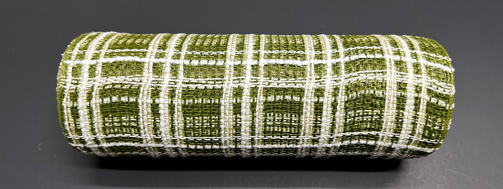 A rolled-up piece of 10X10Y Moss Jute-Cream Fuzz Plaid Mesh XB105210-08 rests on a smooth, dark surface. This jute-like material has a green and white plaid grid pattern that creates a textured look.