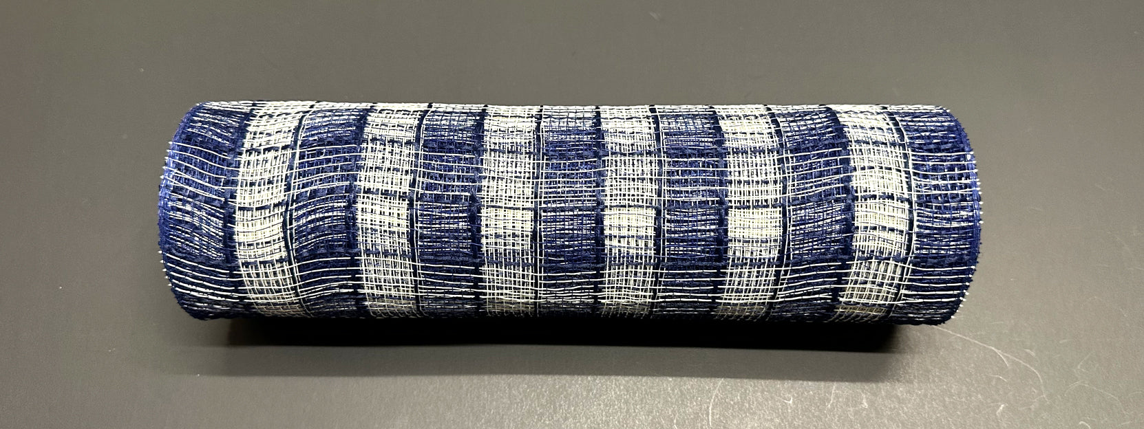 A 10X10Y Navy-Cream Small Chex Plaid Mesh XB235510-27 cylindrical object is on a dark gray surface.