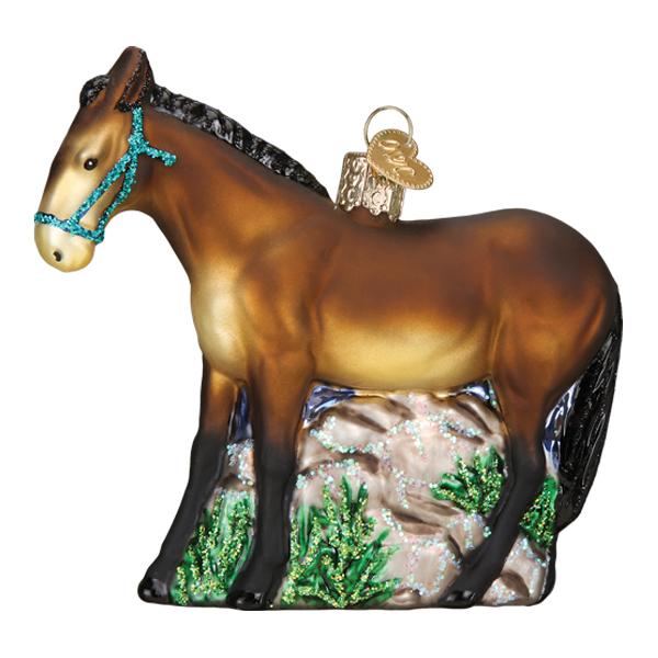 A glass Mule Ornament (Old World Christmas 12582) shaped like a brown mule with a blue bridle, standing on green grass and rocks, finished with a gold ornament cap.