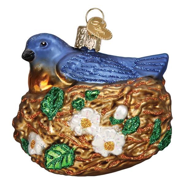 The Bird in Nest Old World Christmas Ornament 16130 is a hand-painted glass bluebird on a golden nest, featuring white flowers, green leaves, and a gold cap with loop for hanging.