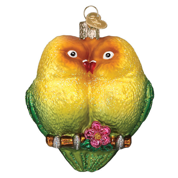 The Lovebirds Ornament by Old World Christmas (16145) features two yellow and green lovebirds snuggled on a branch with a glittery pink flower and gold cap—a charming symbol of love for any space.