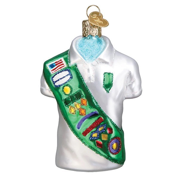 The Girl Scout Uniform 32449 Old World Christmas Ornament is a glass decoration featuring a white shirt with a green sash and colorful badges, perfectly capturing the look of a classic Girl Scout uniform.