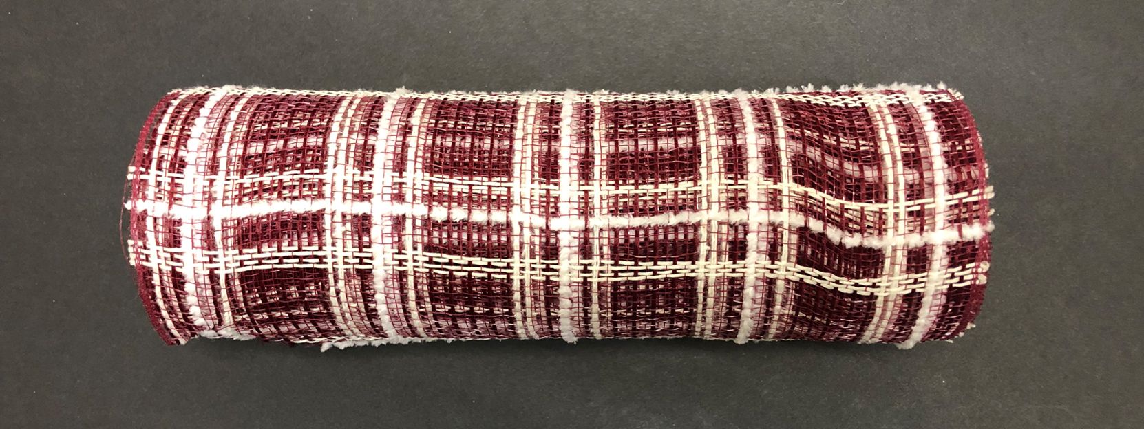 A rolled-up Burgundy Jute-Cream Fuzz Plaid Mesh (10x10Y, XB105210-10) with a burgundy and cream plaid pattern rests on a dark surface, showcasing its textured, woven polyester appearance.