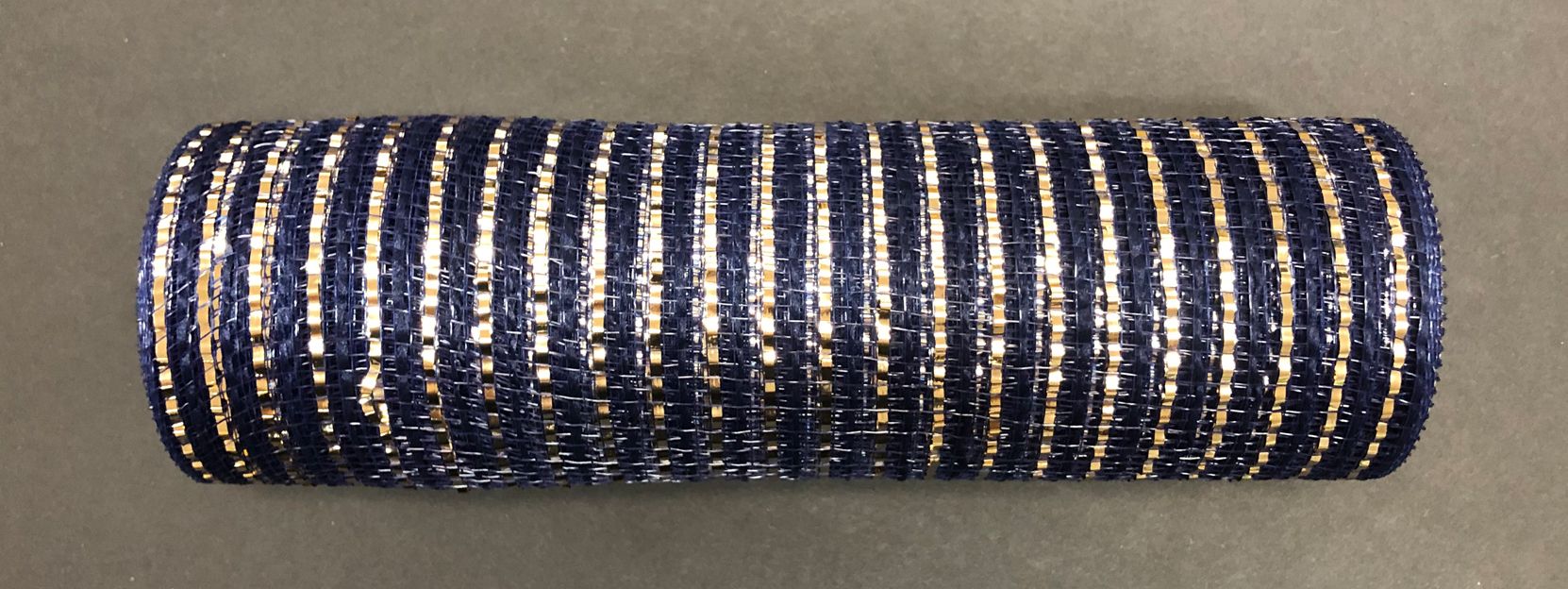 The Navy Fabric Mesh/Champ Stripes, 10X10Y Mesh (XB103410-27), features navy blue, gold, and silver stripes. Made from polyester, this decorative mesh ribbon has a shiny, textured appearance that beautifully catches the light as it rests on a flat surface.