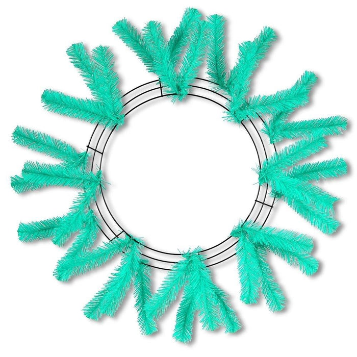 The 24 Work Wreath Seafoam XX748870 features a metal wire base with mesh netting and is adorned with vibrant turquoise artificial pine branches. The branches are evenly arranged in a circular pattern, creating an eye-catching sunburst design perfect for holiday decor.