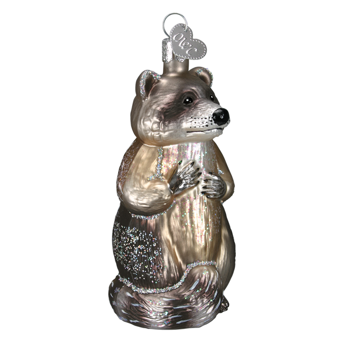 The Raccoon 12146 Old World Christmas Ornament is crafted from glass with metallic and glitter accents, and includes a silver tag at the top for easy hanging.
