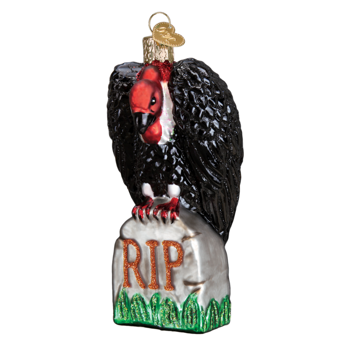 The Halloween Vulture 26082 Old World Christmas Ornament features a vulture perched on a gray tombstone marked “RIP” in orange, with green grass accents.