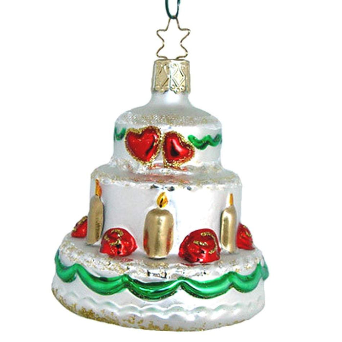 The Wedding Cake Christmas Ornament Inge-Glas of Germany 3-208-05 is a German glass ornament shaped like a tiered white cake with red hearts, gold candles, green trim, and topped with a gold cap and star-shaped hook.