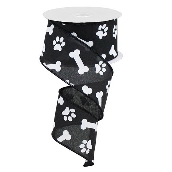 A spool of 2.5 Black with White Paw Prints & Bones Ribbon RGA115102, featuring white paw prints and dog bones, is partially unrolled in a spiral shape.