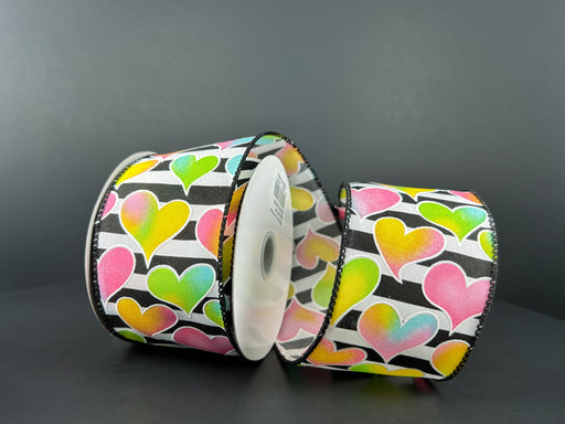 Against a dark backdrop are three rolls of Black and White Satin Stripe Ribbon, featuring 2.5X10Y Pink-Yellow-Blue-Green Ombre Hearts patterns in vibrant colors, creating a striking visual effect.