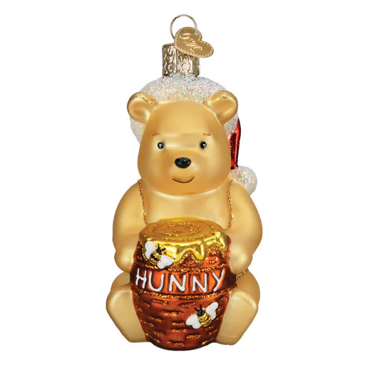 The delightful Winnie the Pooh Old World Christmas 12703 ornament showcases a bear-shaped decoration inspired by the beloved character, adorned with a Santa hat and a honey pot labeled "Hunny." The cheerful bear hangs merrily from its gold hanger, adding festive joy to your holiday decor.