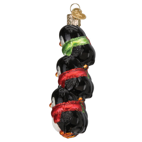 A vertical stack of three penguin ornaments wearing colorful scarves, in the style of a Penguin Family of 9 Old World Christmas Ornament 16156.