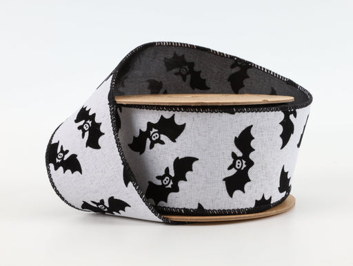 A partially unspooled 2.5" White and Black Glittered Bats with Black Backing Ribbon (6005W-031-63E), featuring a repeating pattern of black bats with white eyes and fangs, is displayed against a plain white background.
