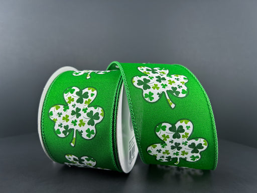 Two rolls of the Emerald Satin/Shamrock Filled Clover 2.5X10Y ribbon display large white shamrocks with smaller green patterns on a dark gray background, emphasizing the intricate Shamrock Clover Ribbon design.