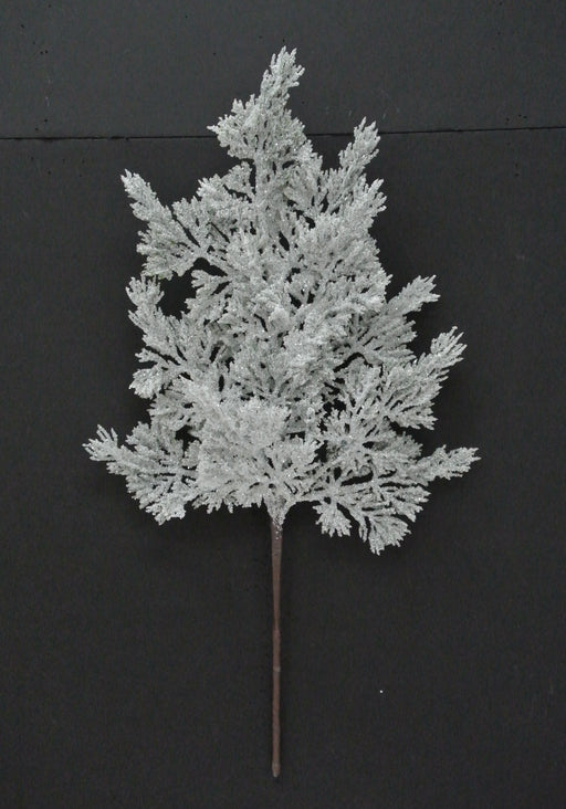 The 20 Green and White Snow Cedar Pick 23007 displays frosted green and white artificial branches with feathery offshoots, dusted in a snowy coating, set against a black background.