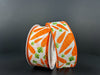 Two rolls of 1.5"X10Y Ivory Linen/Lotsa Carrots Ribbon (31404-09-19) display orange carrots with green leaves on an ivory linen background, upright against a plain dark surface.