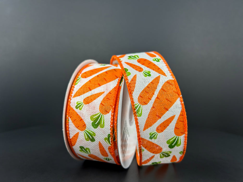 Two rolls of 1.5"X10Y Ivory Linen/Lotsa Carrots Ribbon (31404-09-19) display orange carrots with green leaves on an ivory linen background, upright against a plain dark surface.