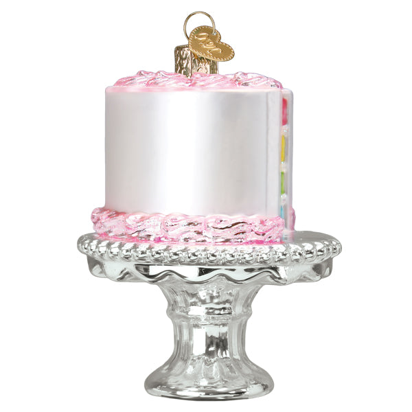 Cake on a Stand Old World Christmas Ornament 32618, shaped like a white cake with pink icing on a silver pedestal stand, featuring a small heart-shaped charm at the top.