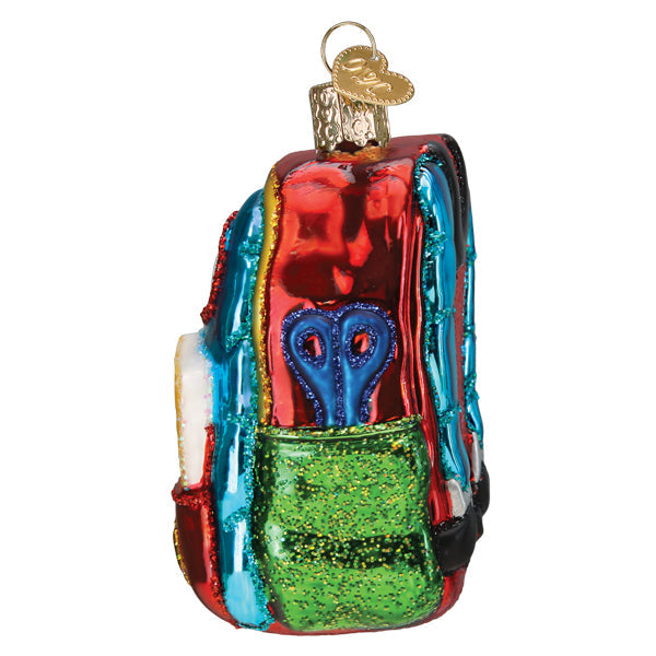 First Day of School Old World Christmas Ornament 32655, a glass ornament shaped like a red backpack with a green glittery front pocket containing blue scissors.