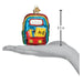 A hand holds a 3.5-inch First Day of School Old World Christmas Ornament 32655, a glass decoration featuring a yellow book labeled A-Z, pencils, and stars.