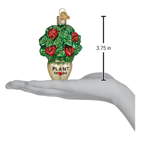 A hand holds a 3.75-inch tall Plant Mom Old World Christmas Ornament 36341, a glass ornament shaped like a potted hibiscus plant with the label PLANT MOM.