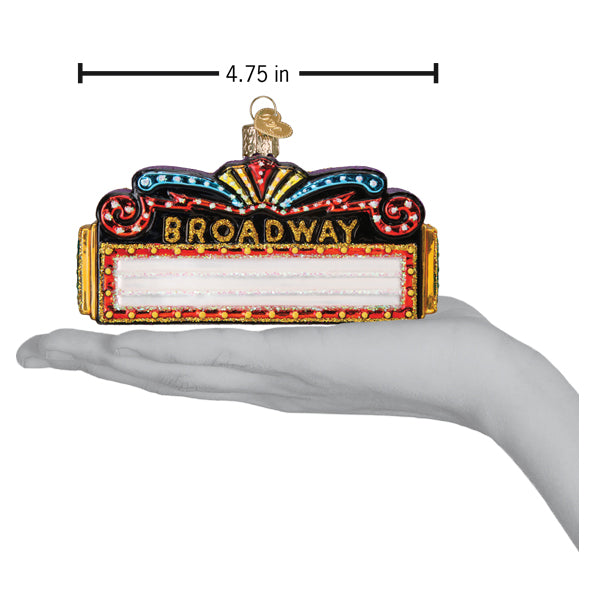 A hand holding a Broadway Marquee Old World Christmas Ornament 36345, shaped like a marquee measuring 4.75 inches across with a blank white sign below the text.