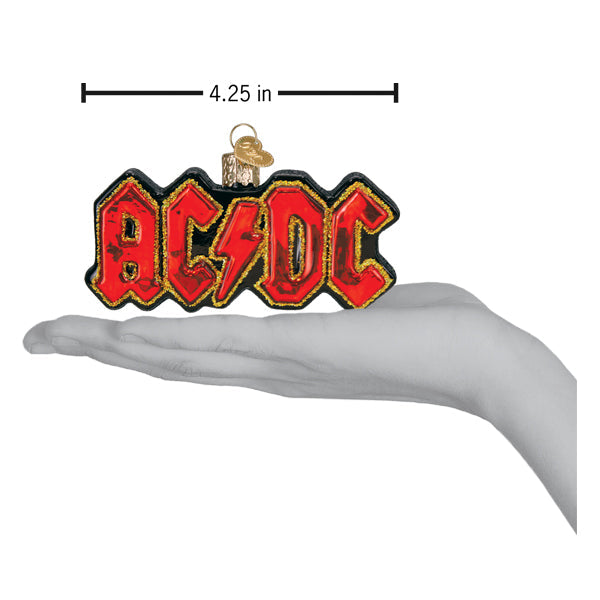 A hand holding an AC/DC Old World Christmas Ornament 38074, a 4.25-inch long glass ornament shaped like a red and black lightning bolt logo.