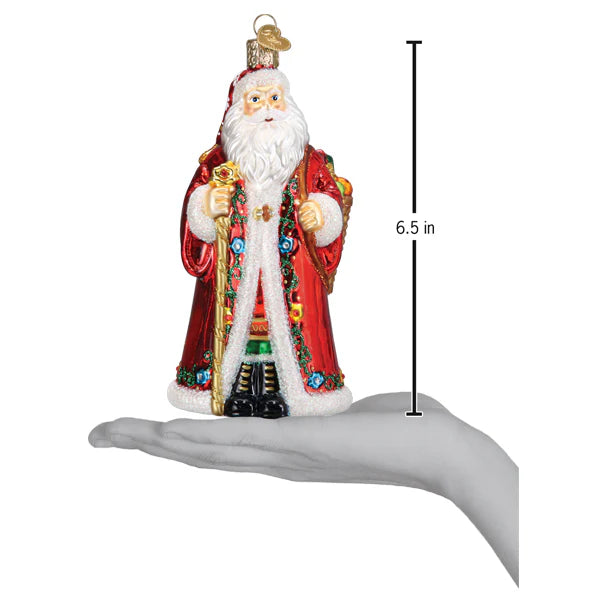 A hand holds a 6.5-inch tall Norwegian Santa Old World Christmas Ornament 40348, featuring Julenisse in a red robe with gold and floral accents, white beard, black boots, and a top hanging loop.