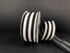 A partially unwound spool of 1.5X10Y Black Linen/White Wide Cabana Stripes Ribbon 41325-09-21 rests on a dark surface, its thick linen boasting bold, evenly spaced stripes against a shadowy backdrop.
