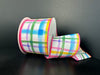 The 2.5X10Y Multi Watercolor Tuttola Plaid Ribbon (41545-40-01) features a colorful plaid pattern with blue, green, yellow, and pink shades on a dark background and has pink edges; it is pictured partly unrolled.