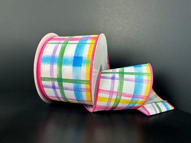 The 2.5X10Y Multi Watercolor Tuttola Plaid Ribbon (41545-40-01) features a colorful plaid pattern with blue, green, yellow, and pink shades on a dark background and has pink edges; it is pictured partly unrolled.