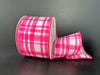 A spool of 2.5"X10Y Pink and White Watercolor Tuttola Plaid Ribbon (41546-40-26) rests on a dark surface, with some of the pink and white ribbon unrolled and folded to the side.