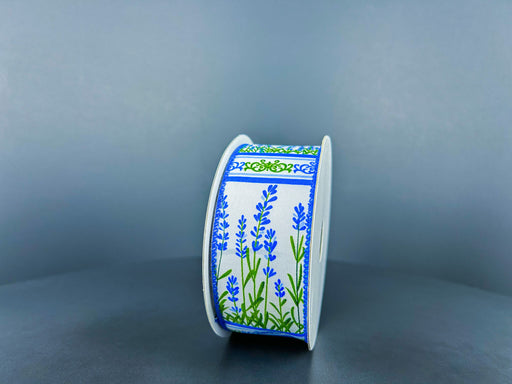 The 1.5X10Y White Satin/Blue Bonnet Garden Ribbon (42411-09-05) stands upright against a gray background, showcasing blue lavender flowers with green stems and bordered by a green and blue ornate pattern on white satin.