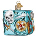 A square, translucent teal Dungeons and Dragons Gelatinous Old World Christmas Ornament 44230 featuring an embedded white skull, a sword, a shield with a red gem, and other adventure gear.