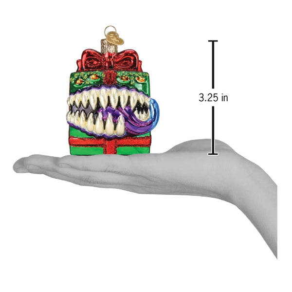 A hand holds a Dungeons and Dragons Holiday Mimic Old World Christmas Ornament 44232 shaped like a green gift box mimic with a gaping mouth filled with sharp teeth and a purple tongue.