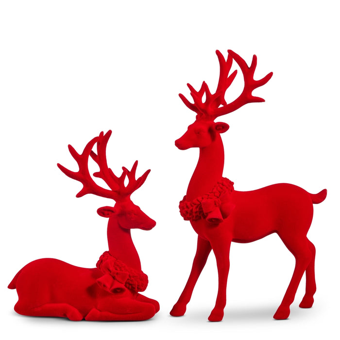 The Set of 2 Red Flocked Christmas Deer (RAZ 4612115) features one standing and one lying down figurine, each with antlers and festive wreaths around their necks, making a charming Christmas accent for your mantel against a white backdrop.