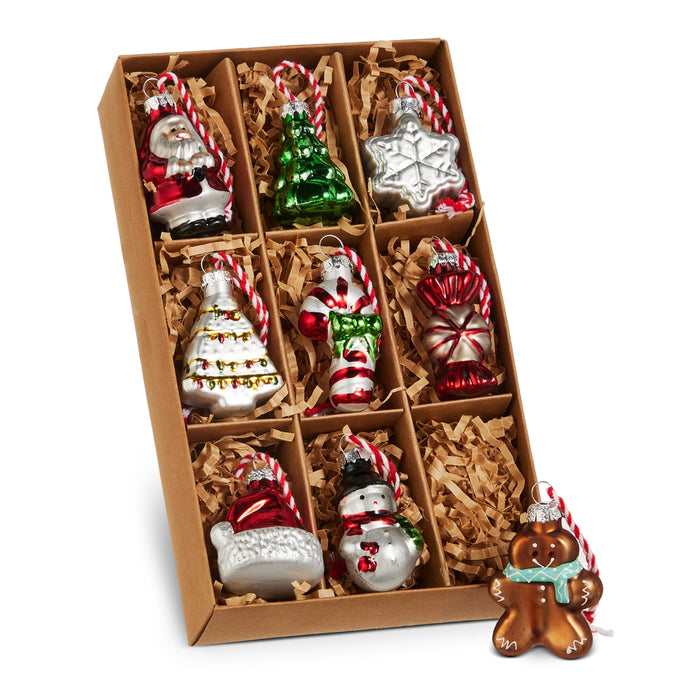 A 2″ box of nine glass Christmas icon ornaments (RAZ 4619184), featuring festive designs like Santa, a tree, a snowflake, and a gingerbread man, beautifully arranged on brown shredded paper.