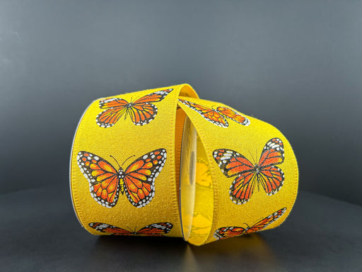 Two rolls of 2.5X10Y Yellow Fuzz Linen/Monarch Butterfly Ribbon 46406-40-22 display bright orange and black butterflies on a gray background. The smooth texture and wired linen design, with one roll slightly unraveling, add charm to any decor project.