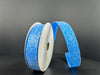 Two spools of 7/8X10Y Turquoise Candy Glittered Satin Ribbon 46420-05-39 are shown on a dark background. One stands upright, the other is unraveled, revealing the glittery texture of the wired satin ribbon.