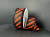 Two rolls of 1.5x10Y OrangeSatin/Black Glitter Diagonal Stripe ribbon with black tinsel edges (51504-09-20) are displayed against a dark background: one upright, the other partially unspooled.