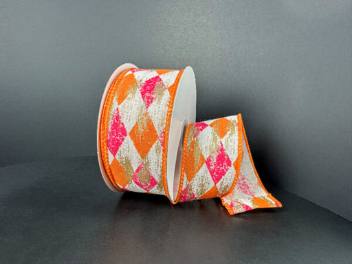 A spool of 1.5X10Y Cream Canvas/Orange-Fuchsia Faded Harlequin/Gold Metallic Ribbon (51505-09-28) sits on a dark surface, with some ribbon unrolled and draped beside it.